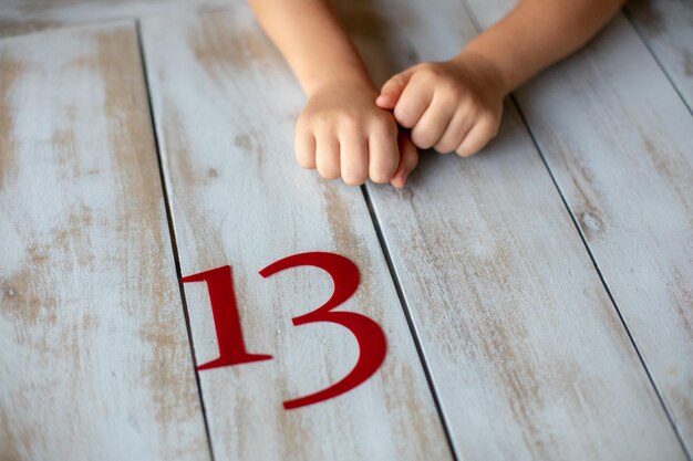 Zdjęcie cyfra trzynasta jest wypisana czerwonymi literami na jasnym drewnianym stole obok dziecięcych rąk.