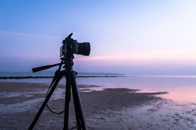 Cyfrowy profesjonalny stojak na aparat cyfrowy DSLR na statywie fotografujący niebo o zmierzchu morskim i fotograf krajobrazu chmur kręci wideo o wschodzie słońca rano podczas odpływu