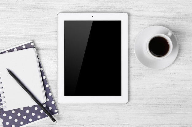 Cyfrowy tablet z filiżanką kawy i notatnikiem na drewnianym stole zbliżenie
