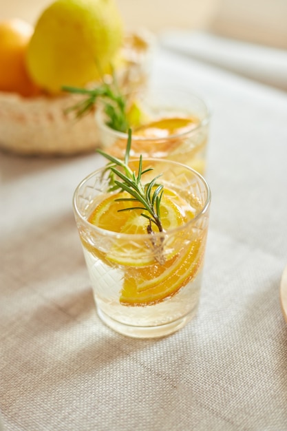 Cytrusy i rozmaryn świeża lemoniada w szkle na białym stole w domu, letni napój, zdrowa woda detox.