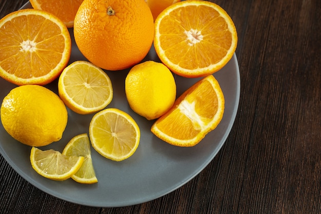 Cytryny i pomarańcze na talerzu na ciemnym drewnianym tle (clouse-up)