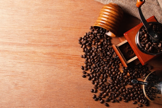 Czajnik do ręcznego młynka do kawy i drewniany kubek z rozsypanymi ziarnami kawy na drewnianym stole Widok z góry