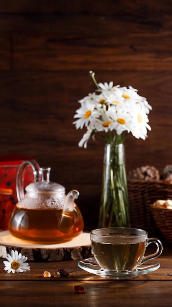 Czajnik i kubek herbaty na drewnianym stole oraz bukiet stokrotek