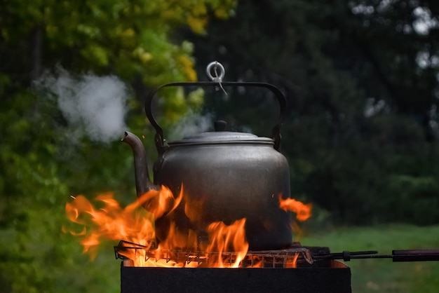 Czajnik kempingowy gotujący się na grillu z parą z dziobka na tle naturalnej przyrody