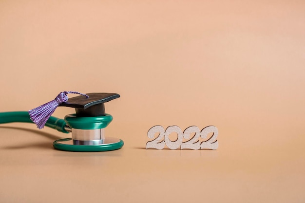 Czapka ukończenia studiów ze stetoskopem i cyframi 2022 na beżowym tle z bliska z kopią miejsca Koncepcja edukacji medycznej
