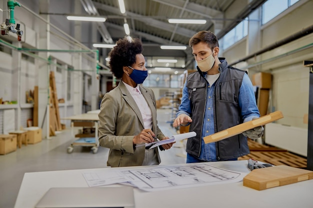 Czarna bizneswoman i stolarz z maskami na twarz rozmawiają o analizowaniu przetworzonego drewna w fabryce