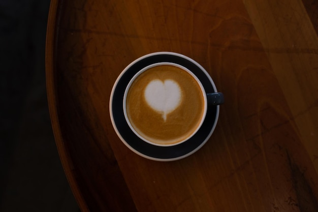 Czarna filiżanka cappuccino z latte art na drewnianym tle