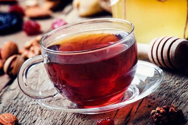 Czarna herbata w szklanym kubku z miodem suszonymi owocami i orzechami słodkie drewniane tło selektywne focus