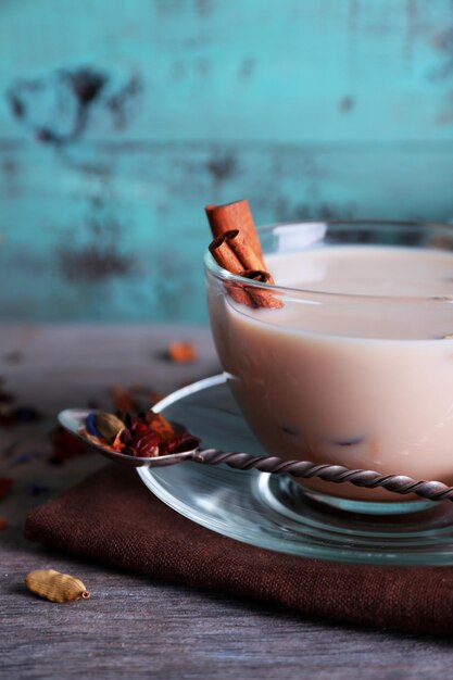 Zdjęcie czarna herbata z mlekiem i cukrem w kawałkach i przyprawami w szklanych naczyniach na kolorowym tle drewnianych desek