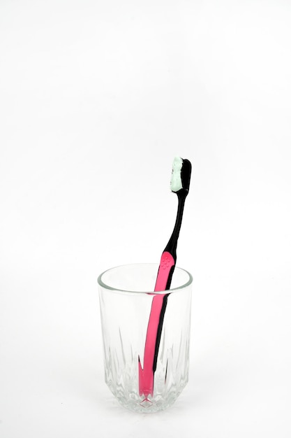 Zdjęcie czarna i różowa szczoteczka z pastą do zębów w szklance izolowanej na białym tle