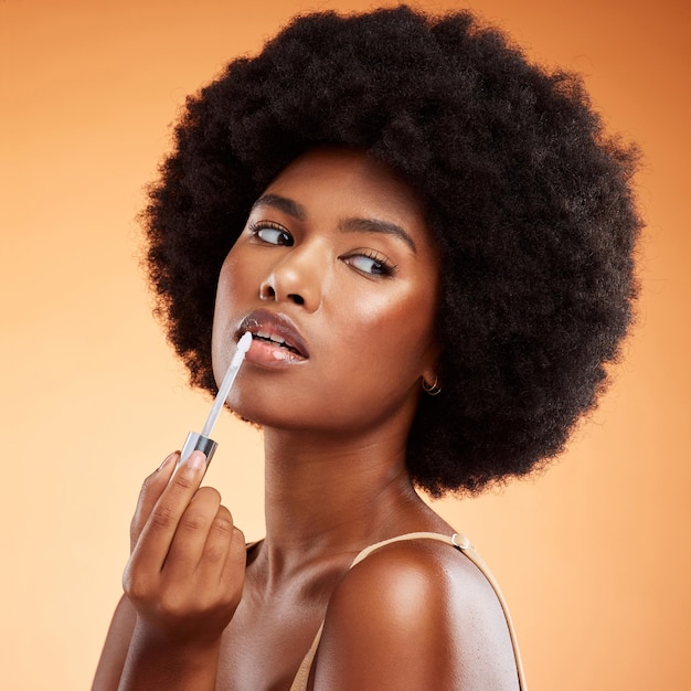 Czarna kobieta afro i naturalne piękno błyszczyk do ust dla zdrowego, błyszczącego i przezroczystego odcienia Kosmetyki nakładają się i piękną twarz afrykańskiej modelki trzymającej narzędzie do makijażu na pomarańczowym tle
