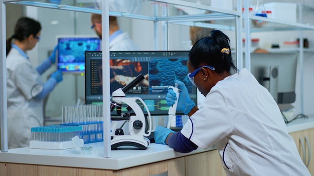 Czarna kobieta chemik analizując reakcję wirusa pod mikroskopem w laboratorium. Wieloetniczny zespół badający ewolucję szczepionek przy użyciu zaawansowanych technologii do badań naukowych, opracowania leczenia przeciw covid19