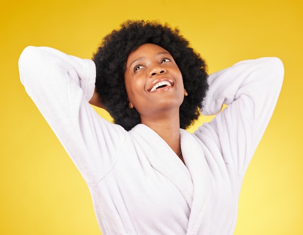 Czarna kobieta relaksuje szlafrok i szczęście w studio gotowym na luksusowy zabieg spa do samoopieki Odosobnione żółte tło i szczęśliwa młoda kobieta z uśmiechem z pielęgnacji skóry i odnowy biologicznej