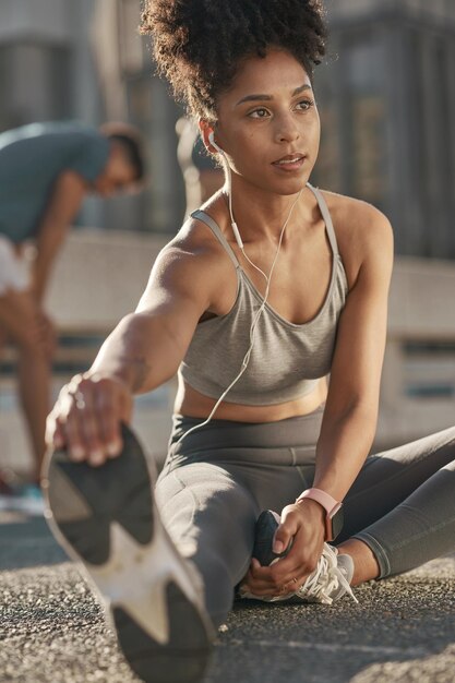 Czarna kobieta rozciągająca nogi i przesyłająca strumieniowo podcast audio joga fitness przed biegiem Trening cardio zdrowy tryb życia i słuchanie muzyki dla motywacji spokój i relaks podczas treningu na ulicy miasta