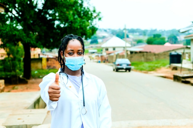 Czarna młoda wspaniała afrykańska pielęgniarka stojąca i podnosząca rękę na kciuki w górę