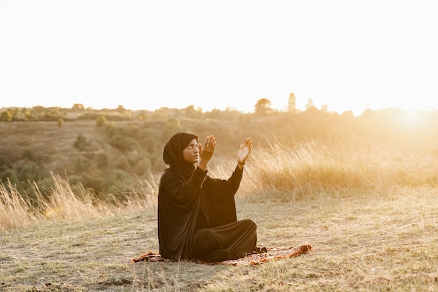 Czarna muzułmanka modli się do Allaha o zachodzie słońca. Solat tradycyjna modlitwa do boga na dywanie.