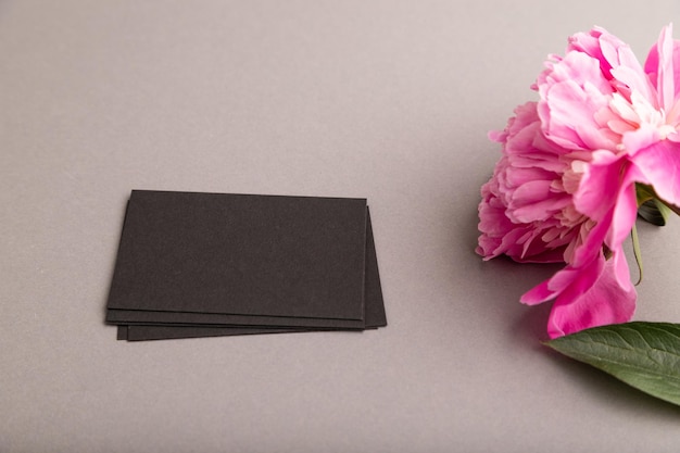 Zdjęcie czarna wizytówka z różowymi kwiatami piwonii na szarym pastelowym tle widok z boku miejsca na kopię