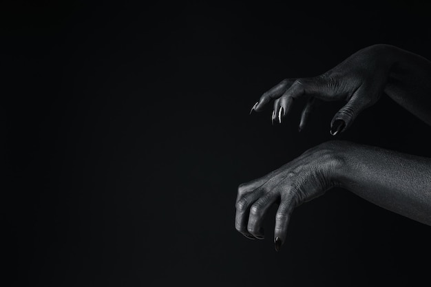 Czarne kobiece dłonie z czarnymi paznokciami na czarnym tle miejsca na tekst