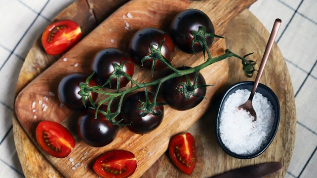Czarne pomidory na gałęzi na drewnianej desce z solą morską