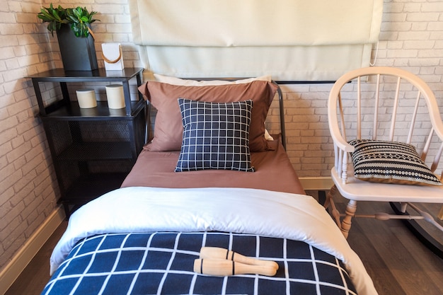 Czarno-brązowa poduszka na brązowym łóżku z czarną stalową półką i drewnianym krzesłem.