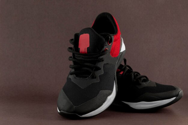 Czarno-czerwone sportowe buty do tenisa na brązowym tle z miejscem na tekst