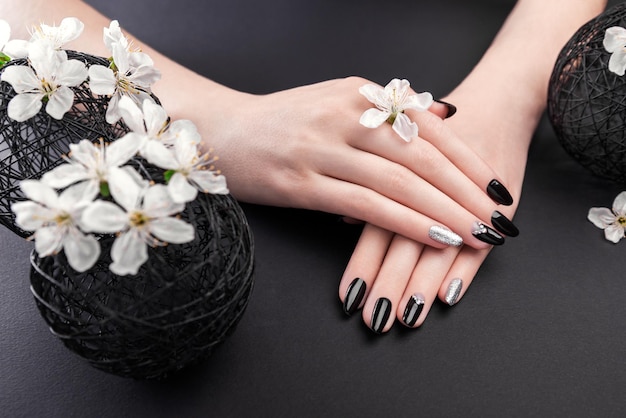 Czarno-srebrny manicure z kwiatem wiśni na czarnym tle Kobieta z czarnymi paznokciami otoczona białymi kwiatami