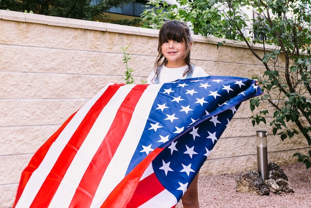 Czarnowłosa dziewczyna trzyma i macha flagą Stanów Zjednoczonych w ogrodzie swojego domu Koncepcja obchodów dnia niepodległości Stanów Zjednoczonych 4 lipca patriotyzm i amerykańska duma