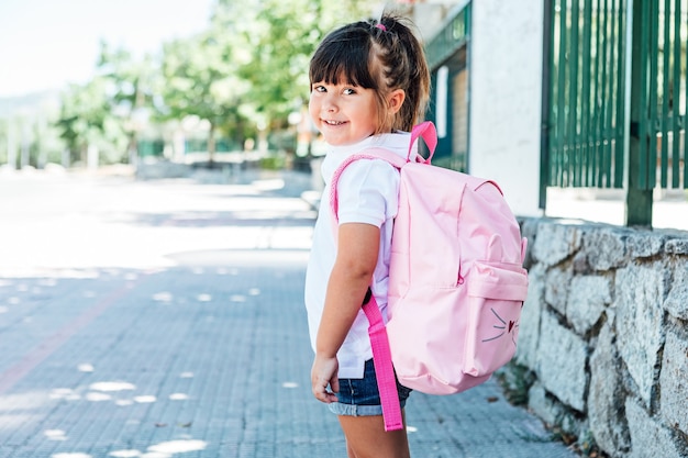 Czarnowłosa dziewczynka ubrana w różowy plecak na ulicy