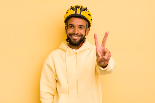 Czarny afro mężczyzna uśmiechający się i wyglądający na szczęśliwego, gestykulując zwycięstwo lub koncepcję roweru pokoju
