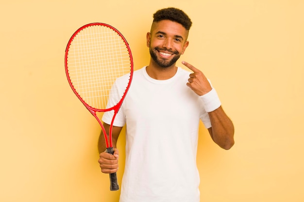 Czarny afro mężczyzna uśmiechający się pewnie wskazując na własną koncepcję tenisa z szerokim uśmiechem