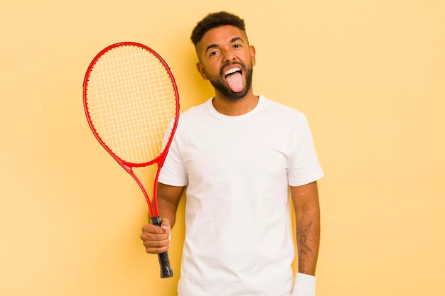 Czarny afro mężczyzna z wesołą i buntowniczą postawą, żartuje i wysuwa język z koncepcji tenisa