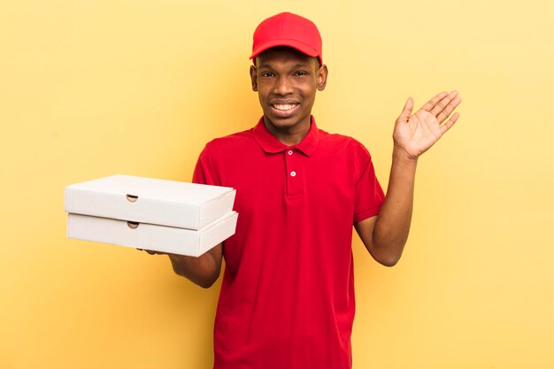 Czarny afro młody człowiek uśmiechający się szczęśliwie machający ręką witającą cię i witającą cię koncepcja dostawy pizzy