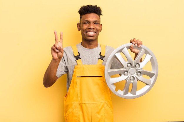 Czarny afro młody człowiek uśmiechnięty i wyglądający przyjaźnie pokazujący koncepcję mechanika samochodowego numer dwa