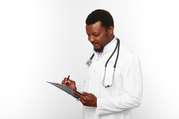 Czarny brodaty lekarz mężczyzna w białym fartuchu ze stetoskopem wypełniającym dokumentację medyczną w schowku