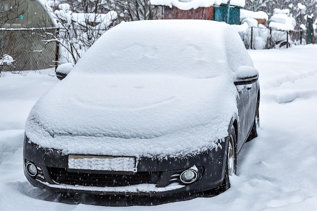 Czarny brudny samochód pod śniegiem Silne opady śniegu Zamarznięty samochód w zaspie zimowe problemy odpala silnik