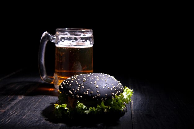 Czarny burger i szklankę piwa na czarnym tle. nieostrość. selektywne skupienie.