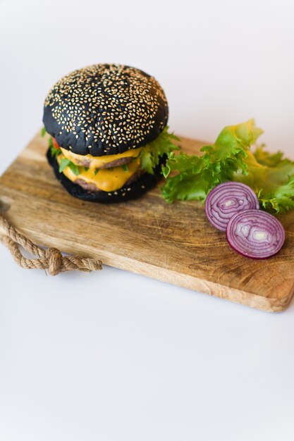 Czarny cheeseburger na drewnianej deski do krojenia, szare tło.