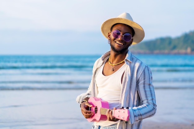 Czarny etniczny mężczyzna cieszy się wakacjami na plaży, grając w ukulele nad morzem