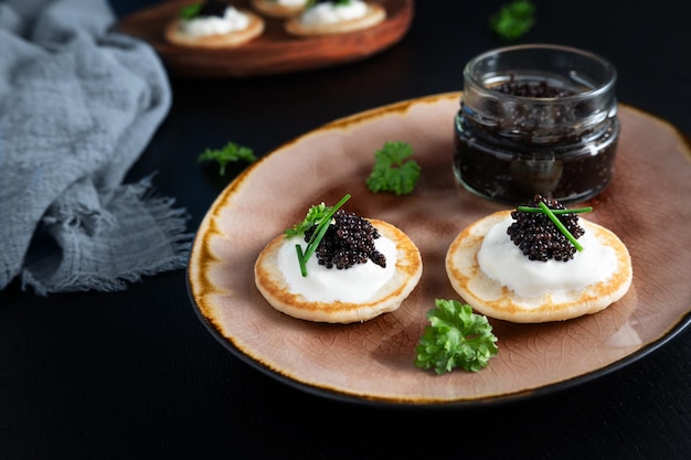 Zdjęcie czarny kawior z jeseterów na mini naleśnikach blinis z kwaśną śmietaną i szklanym słoikiem