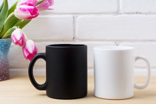 Czarny kubek kawy i biała makieta filiżanki cappuccino z różowymi tulipanami