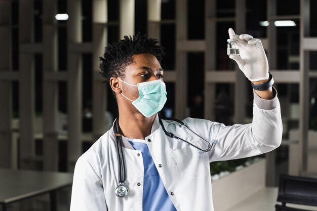 Czarny lekarz z 2 dawkami szczepionki Szczepienie przypominające Afrykański lekarz w masce medycznej trzyma szczepionki w ręku