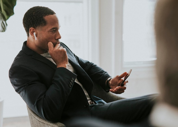 Czarny mężczyzna noszący bezprzewodowe słuchawki i używający swojego smartfona