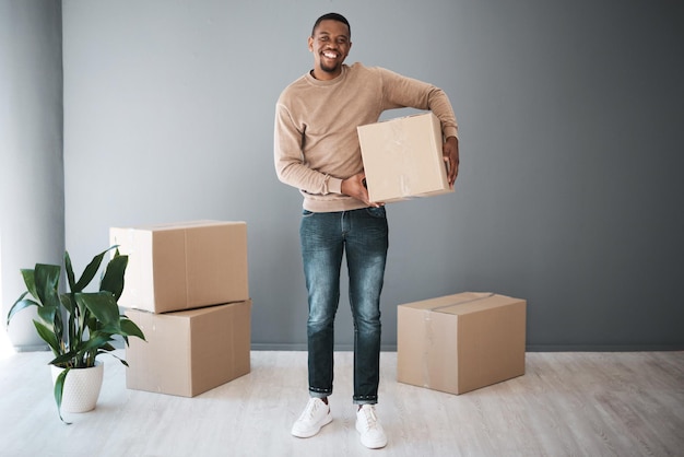 Czarny mężczyzna w ruchu i portret domowy z pudełkiem podekscytowanym nieruchomością i nowym domem Pudełka szczęśliwe i uśmiech właściciela domu stojącego z kartonowymi pudełkami na makiecie reklamowej szarej ściany
