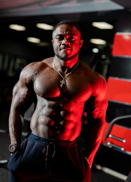 Czarny model kulturysta pozuje przed kamerą w nowoczesnej siłowni Afroamerykanin bez koszulki z silnym abs i idealnym ciałem
