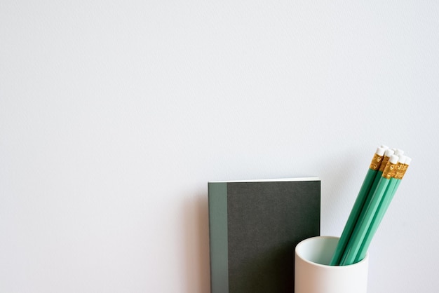 Zdjęcie czarny notebook i zielony ołówek w uchwycie białe tło na ścianie minimalizm przestrzeń do kopiowania