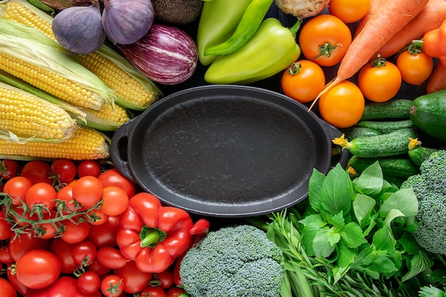 Czarny pusty talerz na tle świeżych, jasnych organicznych warzyw.
