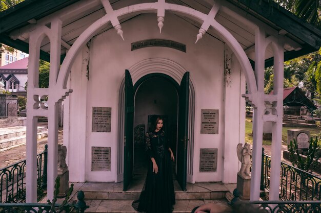 Czarownica w czarnej sukni i strasznym makijażu stała przy bramie cmentarza