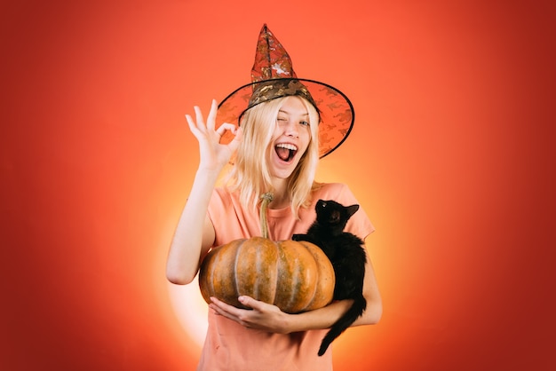 Czarownica z kostiumami dyni i czarnego kota oraz kapeluszami wiedźmy reklamująca koncepcję halloween z izolat...