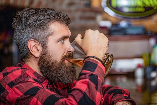 Czas na piwo Mężczyzna pije piwo przy barze Rekreacja stylu życia ludzi Mężczyzna z piwem Brodaty hipster trzyma szklankę piwa Pub piwny Stylowy facet w kawiarni pubie