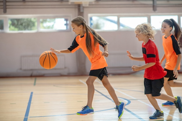 Czas na sport. Dzieci w jasnych strojach sportowych grają razem w koszykówkę i czują się pełni energii